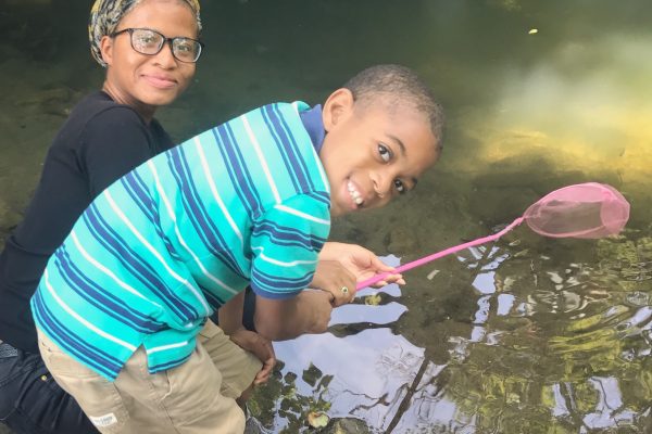 A watershed fellow and a young child hold a net over Cobbs Creek.