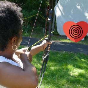 woman draws back arrow, pointed at heart shaped target