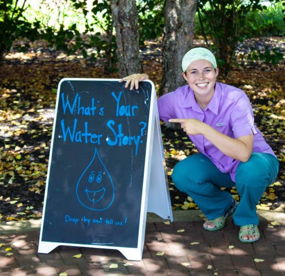 Girl crouches by sign "Whats your water story"
