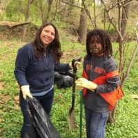 2 individuals clean up trash in a wooded area
