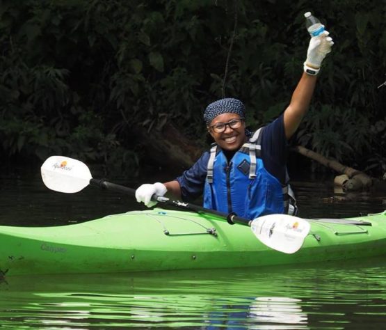 a Fellow kayaks through water on a cleanup, holding a piece of plastic litter