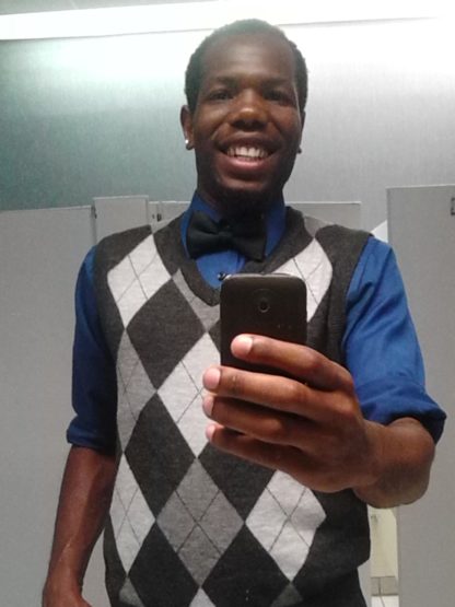 Kamar smiles for a cell phone selfie, wearing an argyle sweater vest