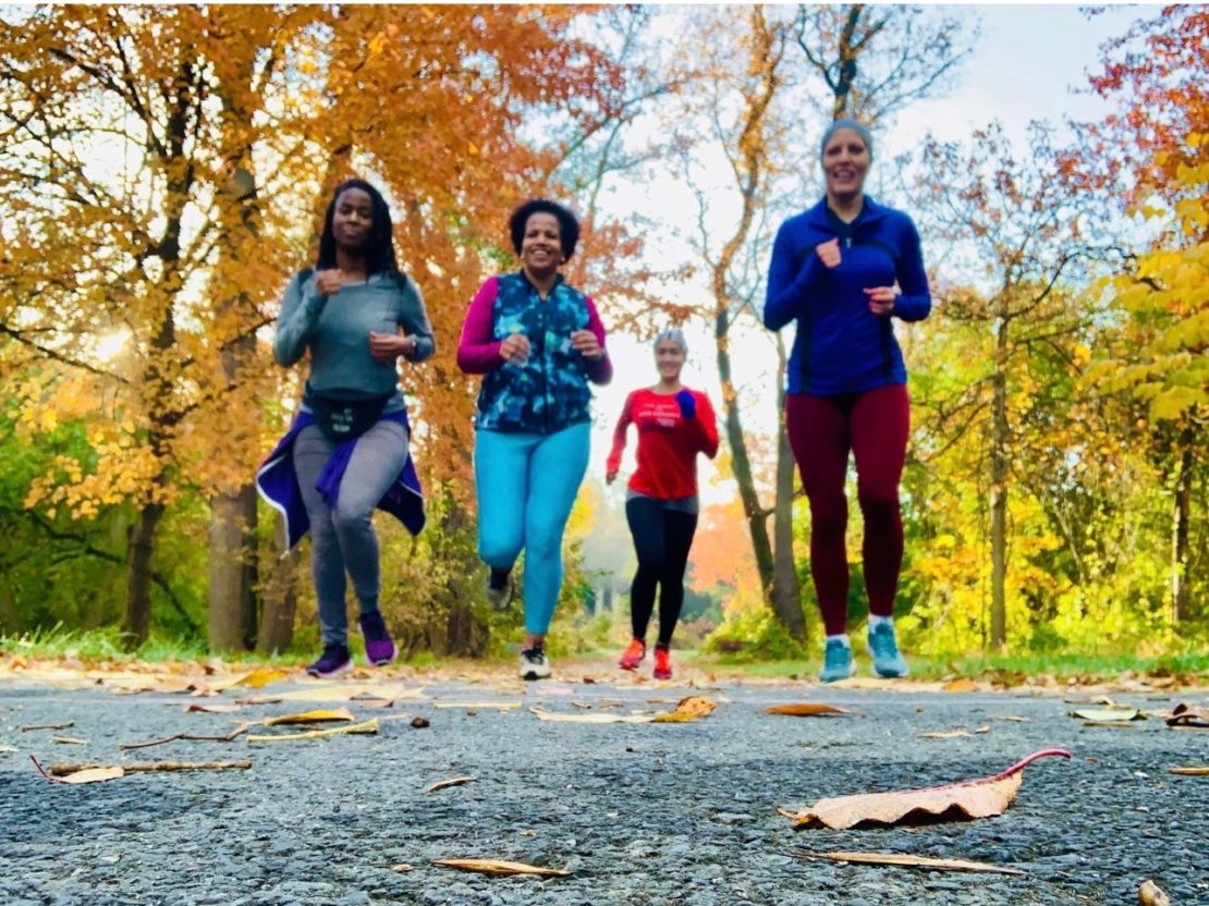 a diverse group of runners run toward the camera on a paved trail